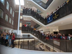 women from many Midwest schools stand behind their schools' banners on a stair case where the conference was held