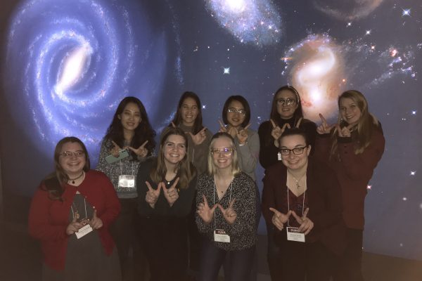 group photo with everyone giving a W sign with their hands, in front of a galaxy-themed backdrop