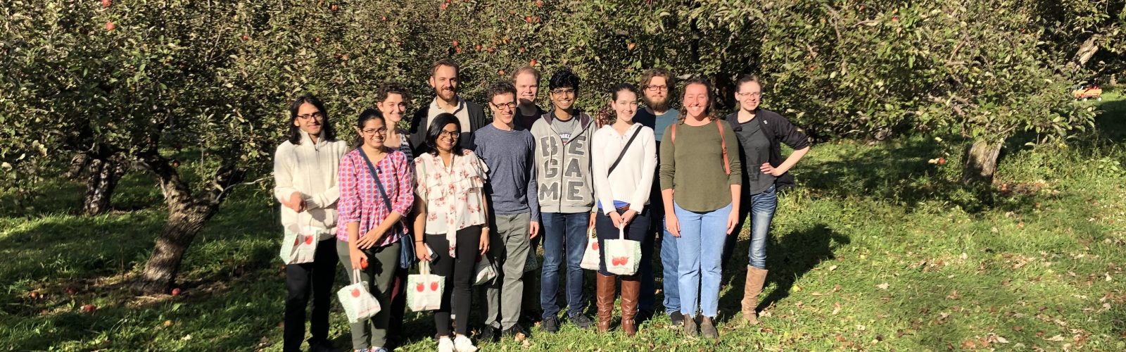 a group of students standing in front of trees at an apple orchard