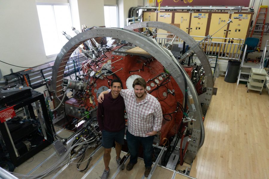 two graduate students stand in front of the Big Red Ball, a large spherical instrument painted red
