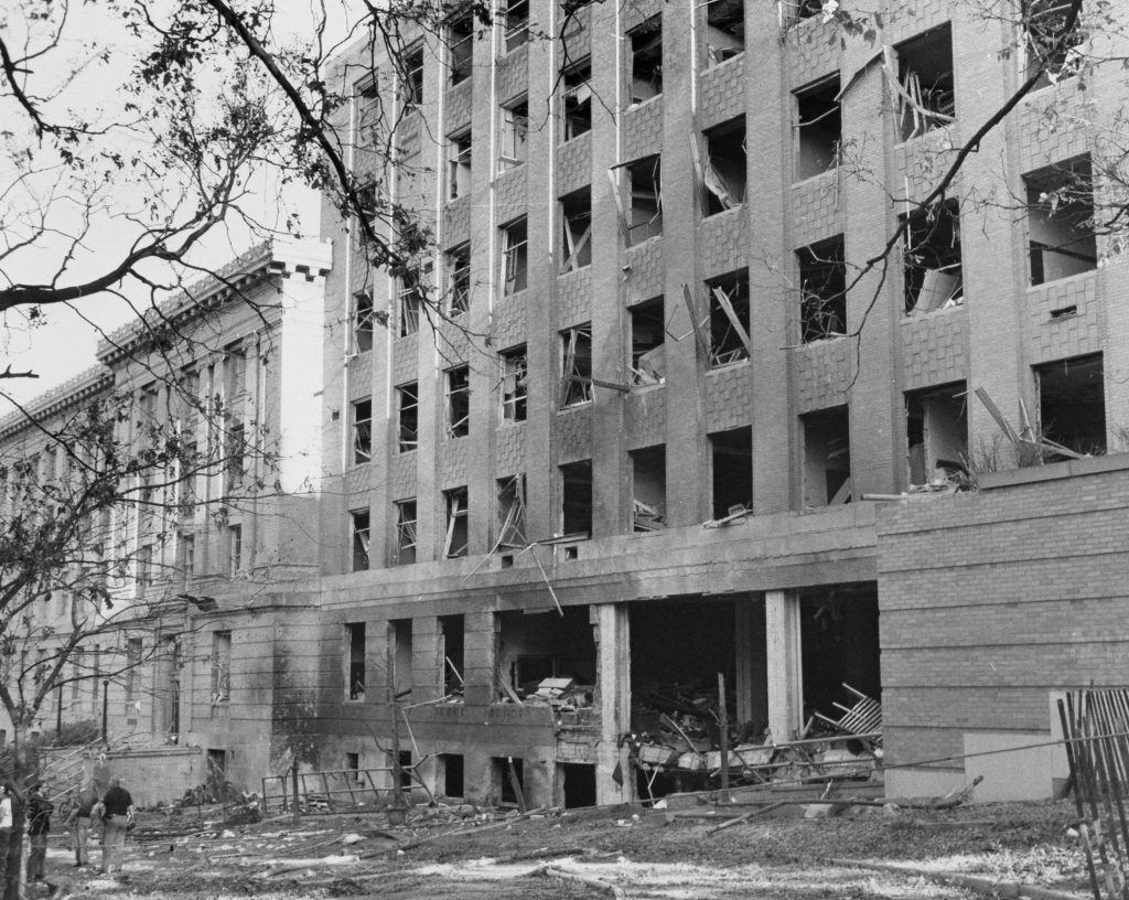 black and white photo of Sterling Hall after the bombing shows a building with windows blown out and obvious damage.