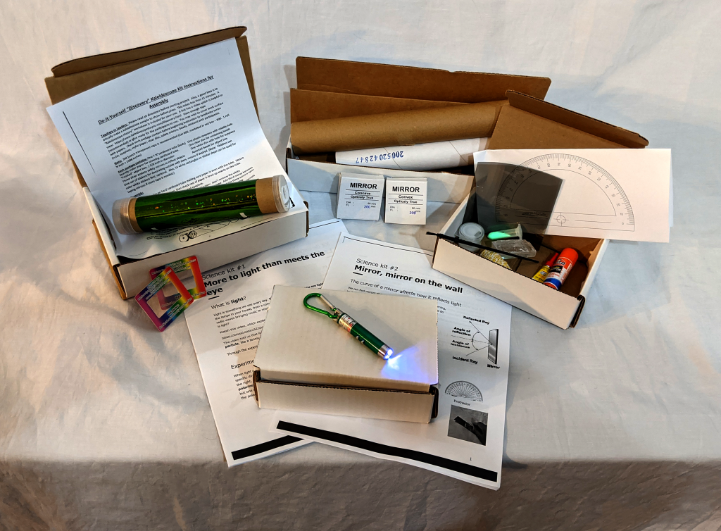 the 4 kits sent home with the students are laid out and opened up, revealing contents like worksheets, laser pointers, mirrors, and lenses