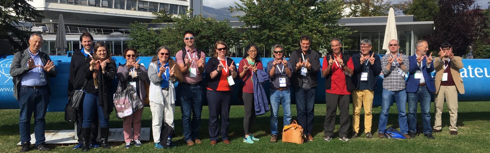 a group of people outside standing in a line making Ws with their hands