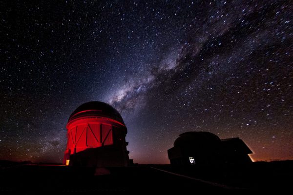 a dimly-lit domed-top observatory on the left at night, with the glow of the milky way visible in the sky above it
