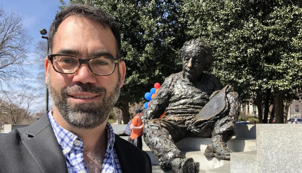 Kyle Cranmer stands next to a statue of Einstein sitting