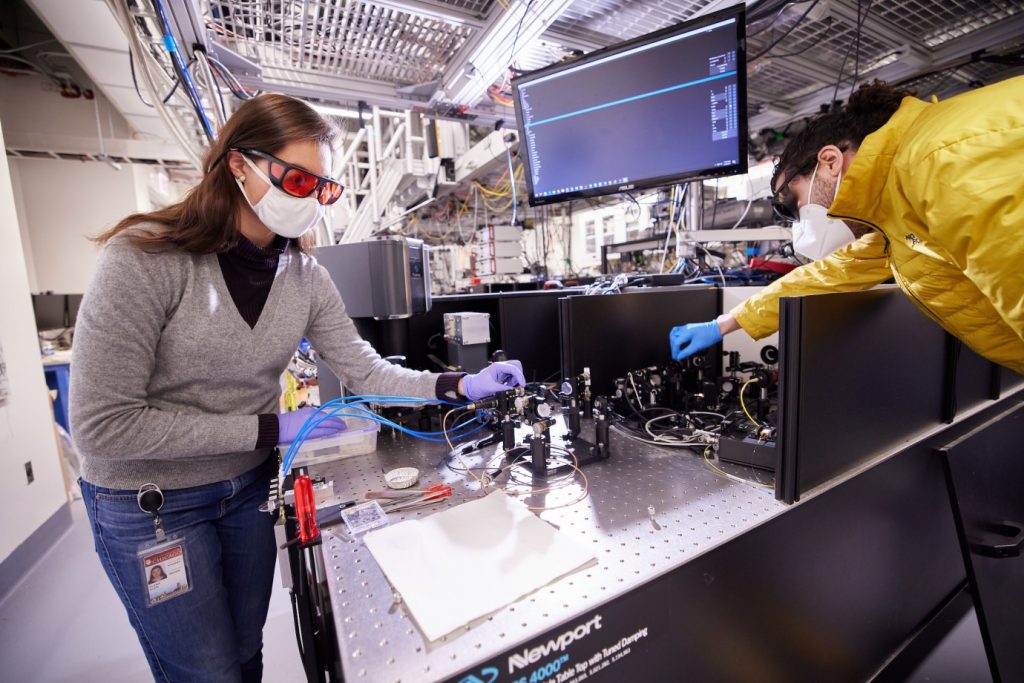 a woman and a man in an optics lab adjust wiring and mirrors