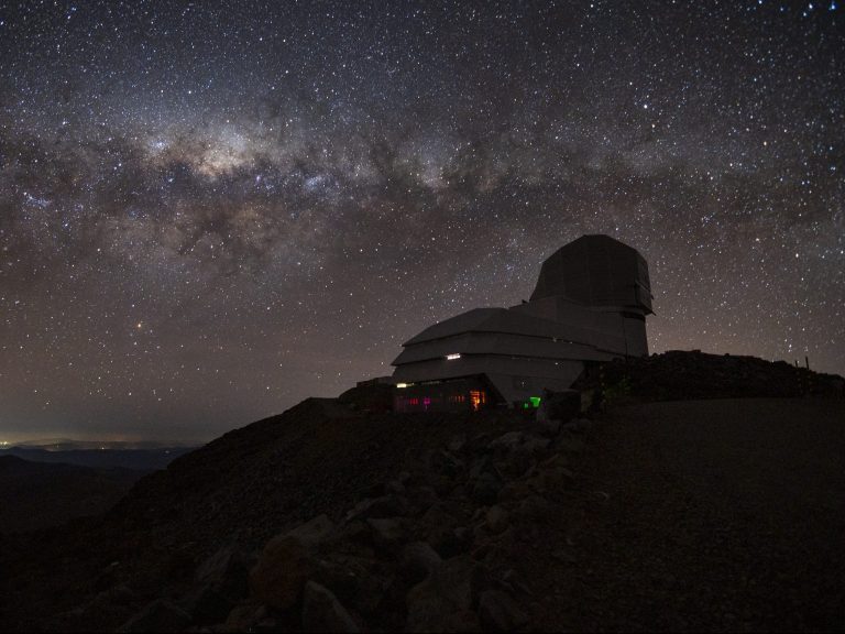 a cosmology research observatory on top of a hill at night, with the Milky Way visible in the night sky