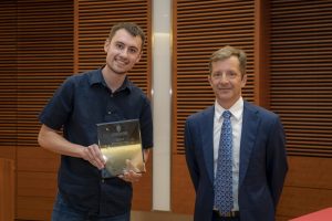 two men stand next to each other, the one on the left is holding a plaque