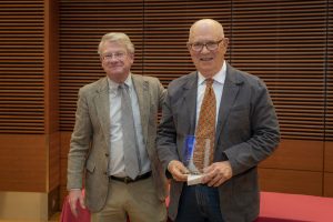 two men stand next to each other, one holding a plaque