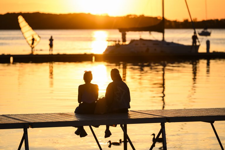 Two people sitting on a dock at Lake Mendota at sunset