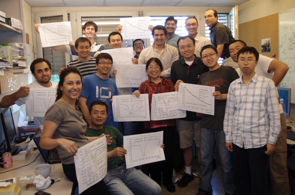 a group of very happy scientists pose for a shot, all holding a printout of the same graph