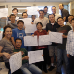 a group of very happy scientists pose for a shot, all holding a printout of the same graph