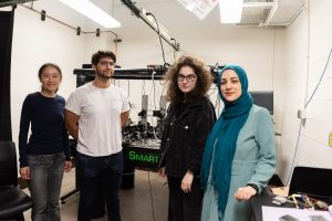 Four people stand in a lab in front of electronics equipment