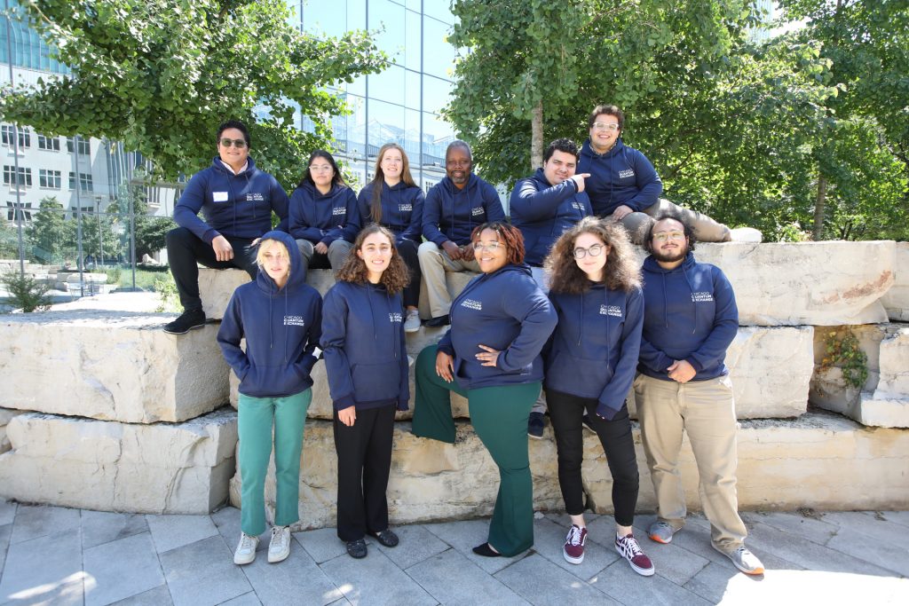 11 students pose on a rock wall, all students are wearing the same Chicago Quantum Exchange hooded sweatshirt
