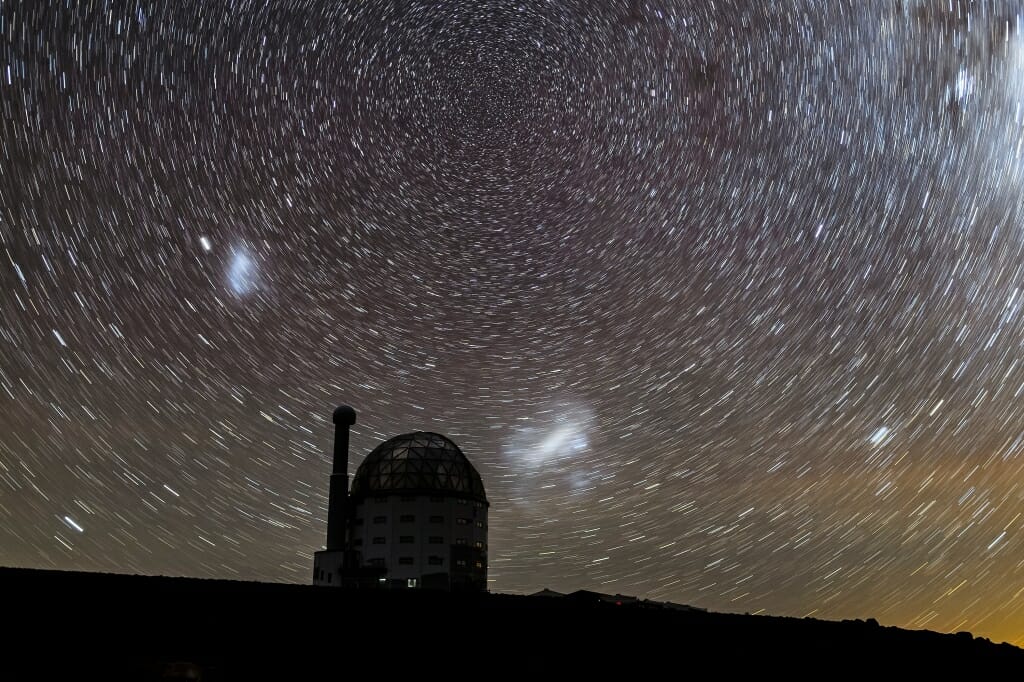 a domed observatory with the night sky as a backdrop. the long exposure makes the stars look like they're rotating, with long blurry tails