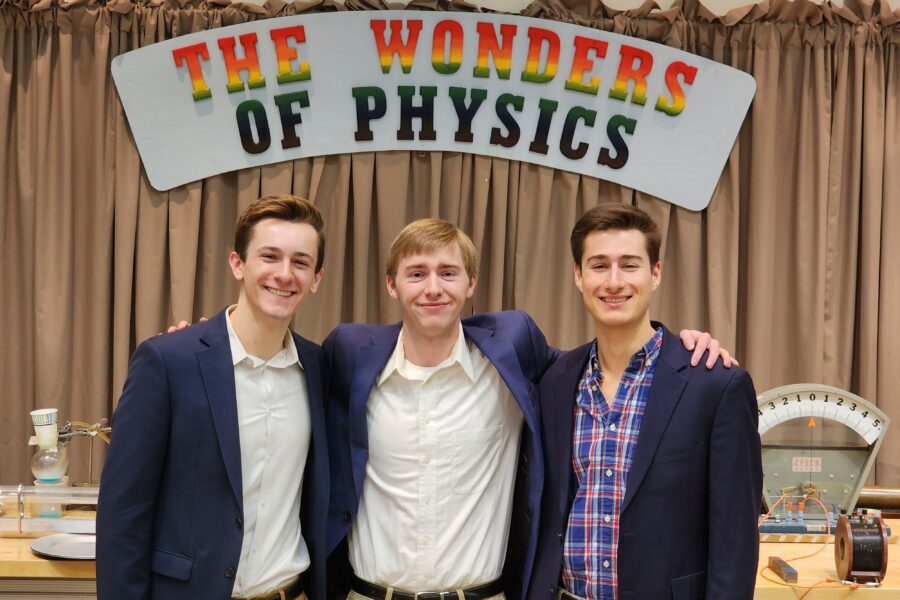Three men in sportcoats stand in front of a sign that says The Wonders of Physics