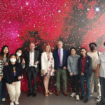 a group of people stand in front of a red, starry-like backdrop