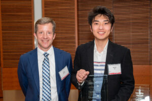 a man on the left with a man on the right holding a clear glass plaque