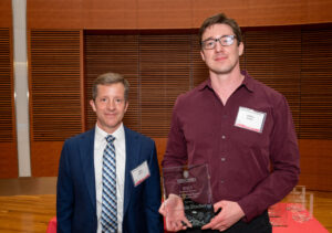 a man on the left with a man on the right holding a clear glass plaque