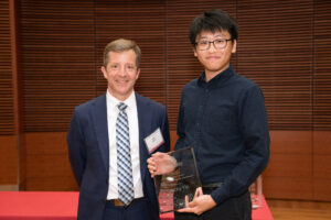 a man on the left with a man on the right holding a clear glass plaque