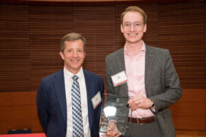 a man on the left with a man on the right holding a clear glass plaque