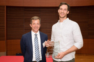 a man on the left with a man on the right holding a clear glass plaque