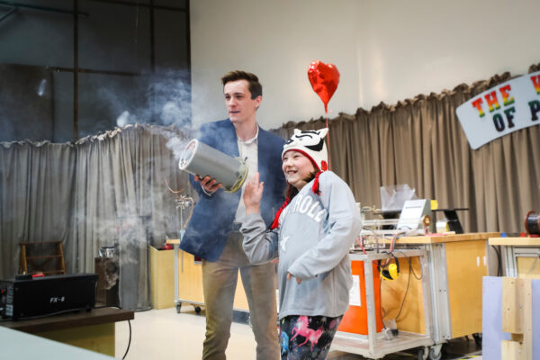 a man and a child demonstrate the vortex cannon, with fog coming out of the cylindrical apparatus in the shape of a ring