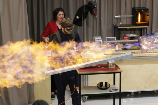 a man stands behind a huge flame with a plastic water jug shooting off to the side