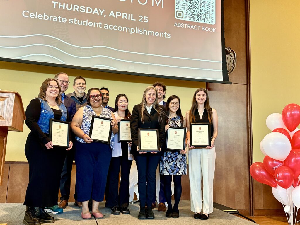 a group of people stand on a stage, all holding framed certificates