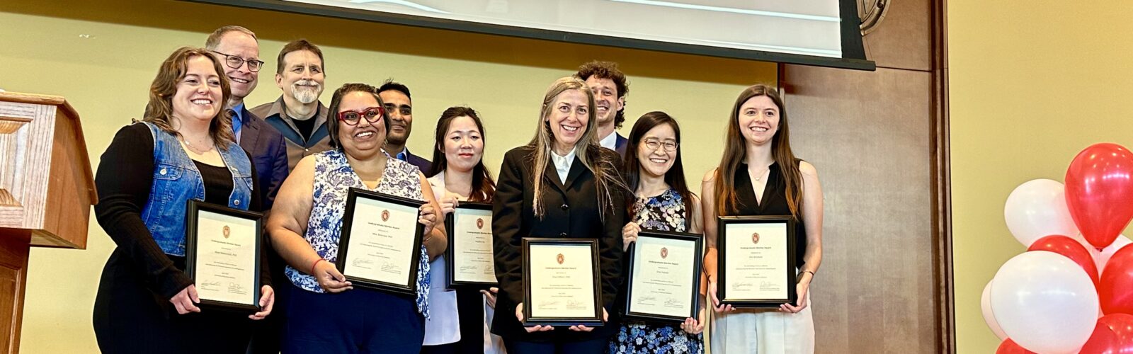 a group of people stand on a stage, all holding framed certificates
