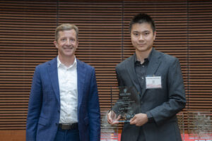 two men stand next to each other, one is holding a glass plaque