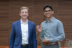 two men stand next to each other and smile, one holds a plaque