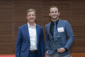two men stand next to each other and smile, one is holding a glass plaque