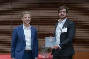 two men stand next to each other and smile, one is holding a glass plaque