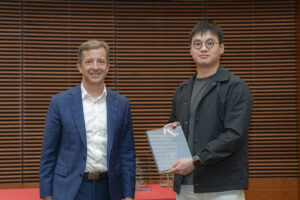 two men pose, one is holding a glass plaque