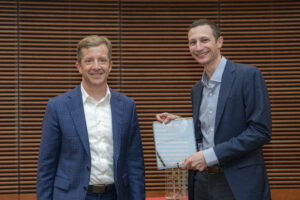 two men smile one is holding a glass plaque