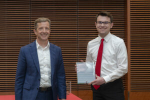 two men smile, one is holding a glass award
