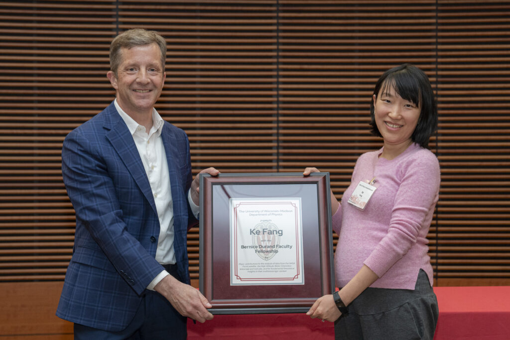 a man and a woman smile while both holding a framed award certificate
