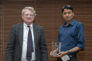 two men pose while one holds a glass award
