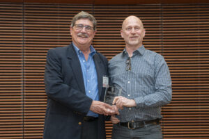 two smiling men hold a glass award