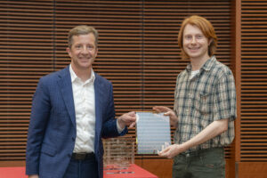 two smiling people hold a glass plaque