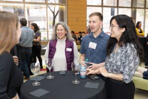 four people stand around a table, one has their back to the camera