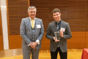 two people stand, one is holding a glass plaque