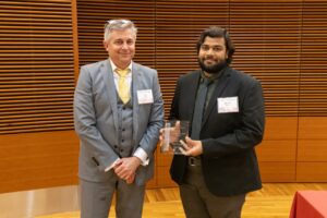 two people stand, one is holding a glass plaque