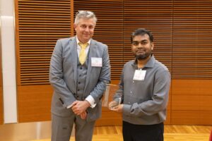 two people stand, one is holding a glass award