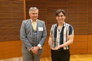 two people stand, one is holding a glass award