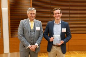 two people stand, one is holding a glass award