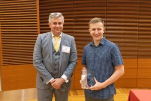 two people stand, one is holding a glass award