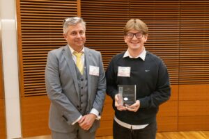 two people stand, one is holding a glass award