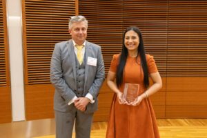 two people stand, one is holding a glass award